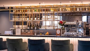 Una zona de bar con mostrador, taburetes y una variedad de botellas y vasos.