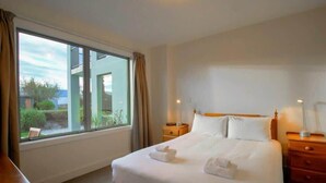 Een hotelkamer met een groot raam, een bed met witte lakens, twee nachtkastjes en een nachtkastje.