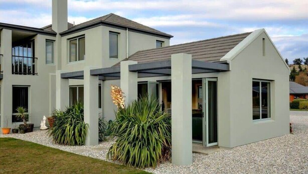 Een modern huis met twee verdiepingen, een overdekte patio, een groot raam en een oprit met grind.