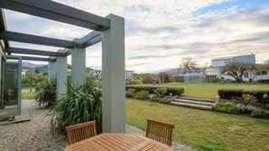 Een overdekt terras met een tafel en stoelen, omgeven door een tuin met uitzicht op een woonwijk en bergen op de achtergrond.
