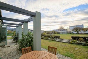 Un espace extérieur aménagé, abrité et doté d’une table et de chaises, entouré d’un jardin offrant une vue sur un quartier résidentiel et, au loin, sur des montagnes.