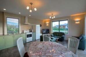 A modern kitchen with a marble countertop, dining area with a table and chairs, a sofa, and a television.