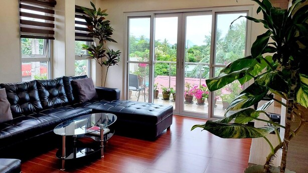 Ein modernes Wohnzimmer mit einer schwarzen Ledersofa, einem Glastisch und großen Fenstern, die einen Blick ins Freie bieten.