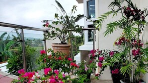 Ein Balkon mit Kübelpflanzen und Blumen, einer Glasreling und Blick auf die umliegende Landschaft.