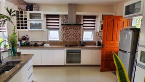 Eine moderne Küche mit weißen Schränken, einer Granit-Arbeitsplatte, einem eingebauten Backofen, einem Kühlschrank und einem Fenster mit Jalousien.