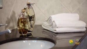 Un ripiano del bagno con un vaso di vetro contenente rami secchi, un asciugamano bianco piegato e un lavandino.