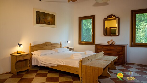 Una camera da letto con un letto di legno, un comodino con una lampada, una cassettiera e una finestra vista verde.