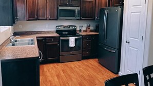 Una cocina compacta con armarios de madera oscura, un refrigerador de acero inoxidable, un microondas y una estufa.