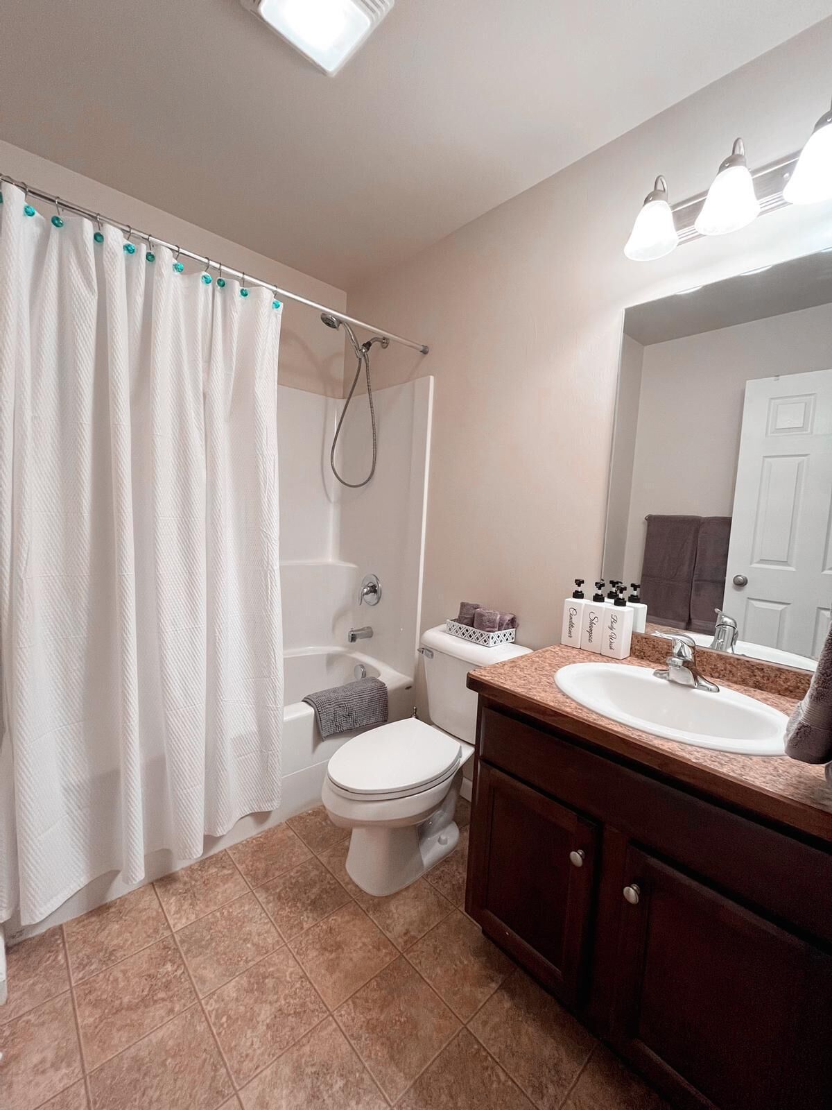 A bathroom with a shower, toilet, sink, and a mirror.