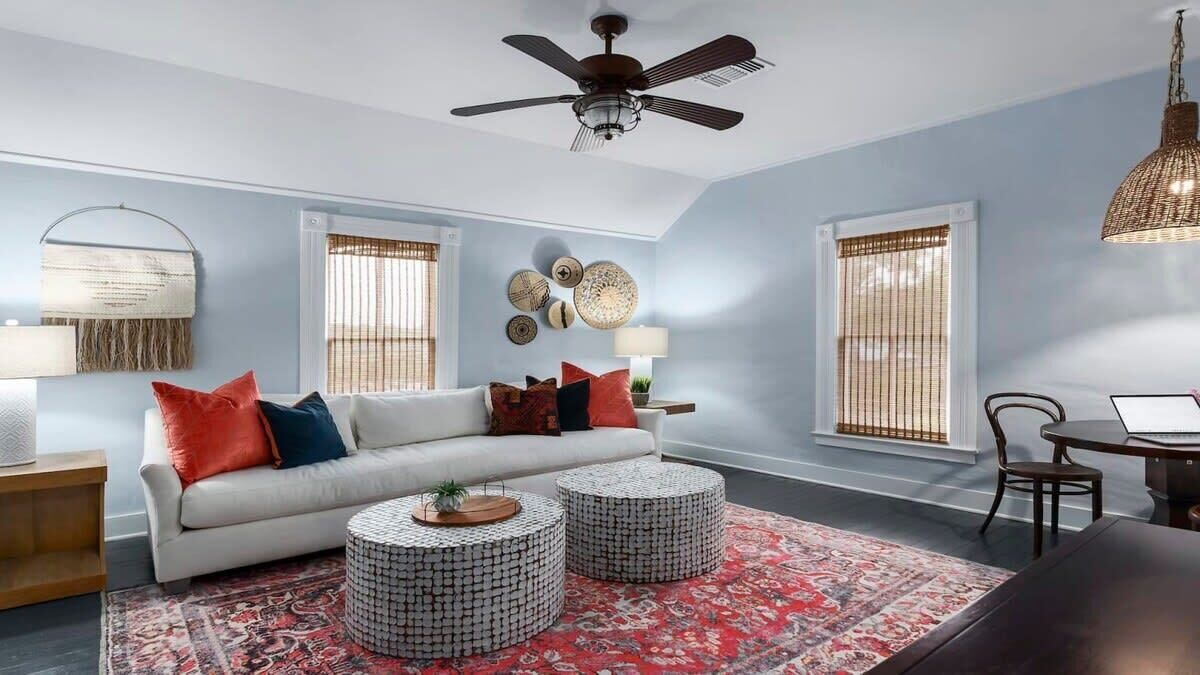 A living room with a white sofa, two round coffee tables, a red patterned rug, and a ceiling fan.