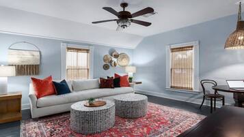 A living room with a white sofa, two round coffee tables, a red patterned rug, and a ceiling fan.