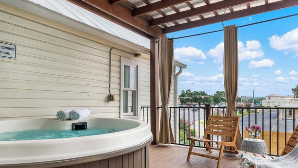 Un balcon abrité avec un jacuzzi, des chaises en bois et une vue sur un parking.