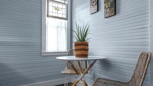 Une pièce avec une table blanche et des chaises en osier, une plante en pot et une fenêtre ornée de vitraux.