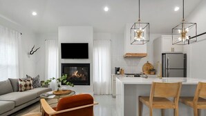 Une cuisine moderne dotée d’un îlot central, de meubles blancs et d’un téléviseur à écran plat fixé au-dessus de la cheminée.