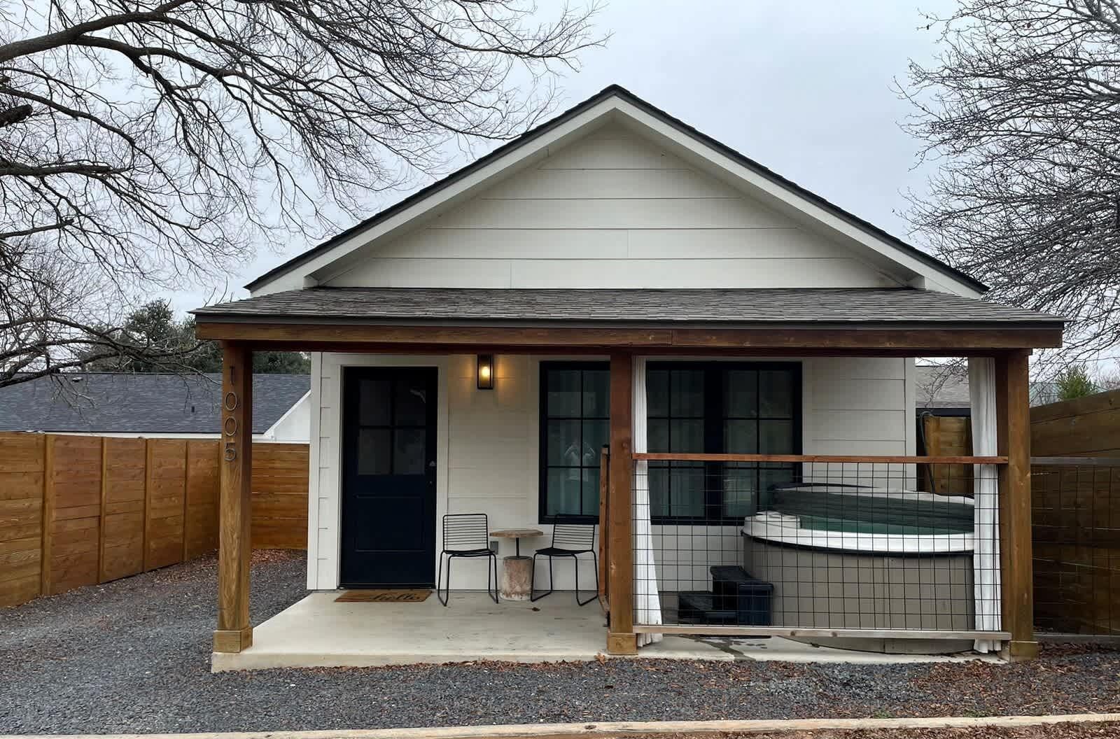 A small house with a covered porch, a hot tub, and a door with a window.