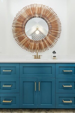 Une salle de bain avec un meuble-lavabo bleu, un miroir rond doté d’un cadre en bois et un mur blanc.