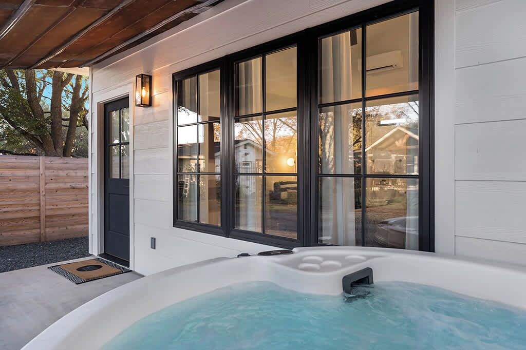 Et moderne udeområde med jacuzzi, træterrasse, store vinduer og en dør.