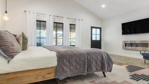 A modern bedroom with a large bed, a flat-screen TV, and a sliding glass door to the outside. - Private guesthouse, Hot tub, soaking tub, In town! (Fredericksburg)