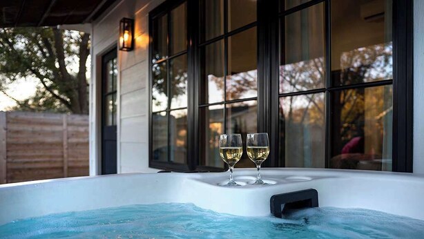 A hot tub with two glasses of wine, surrounded by large windows and a wooden fence. - Private guesthouse, Hot tub, soaking tub, In town! (Fredericksburg)