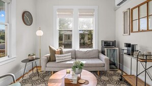 Ein Wohnzimmer mit einer Couch, einem Couchtisch, einer Uhr und einem Fenster mit Jalousien.