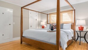 Uma cama de dossel com um cobreleito branco, duas mesas de cabeceira com abajures e uma janela com persianas.