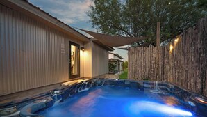 Een hottubgedeelte met een houten terras, een metalen hek en een gebouw met een deur.