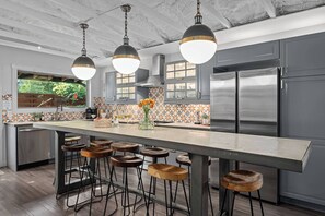 Una cocina moderna con una isla grande, taburetes de bar, electrodomésticos de acero inoxidable e iluminación colgante.