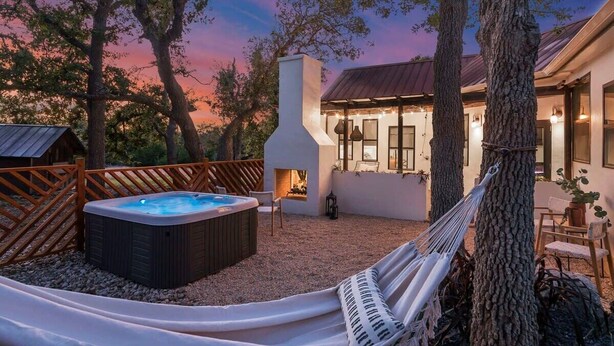 A hot tub, hammock, and outdoor seating area with a view of a house and trees. - Coco Casita, Private Hot Tub, Secluded! (Fredericksburg)