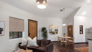 A modern living room with a brown sofa, a wooden coffee table, and a dining area with a wooden table and chairs. - Coco Casita, Private Hot Tub, Secluded! (Fredericksburg)