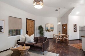 A modern living room with a brown sofa, wooden coffee table, and a dining area with a wooden table and chairs.