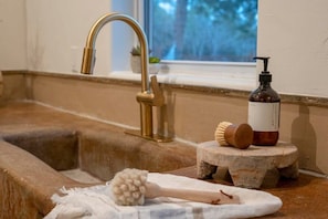 Ein Badezimmerwaschbecken mit einem goldenen Wasserhahn, einer Seifenspender und einer Holzbürste auf einem Stehpult.