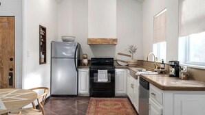 A modern kitchen with white cabinets, a stainless steel refrigerator, a black stove, and a wooden countertop.
