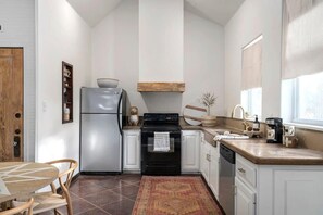 A modern kitchen with white cabinets, a stainless steel refrigerator, a black stove, and a wooden countertop.