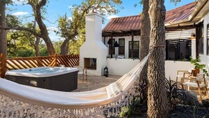 A modern house with a hot tub, hammock, and outdoor seating area surrounded by trees.