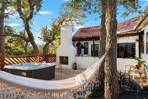 A modern house with a hot tub, hammock, and outdoor seating area surrounded by trees.