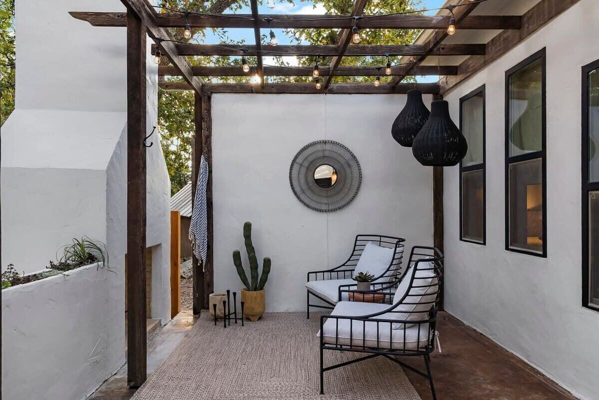 A covered outdoor seating area with a pergola, a round mirror, and hanging pendant lights.