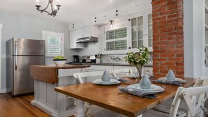 Een moderne keuken met witte kasten, een roestvrijstalen koelkast, een houten eettafel en een wand van baksteen.