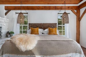 A bedroom with a wooden ceiling, a large bed with a white headboard, two wicker lamps, and a view of greenery outside. - Hot tub, Pet Friendly, Outdoor shower, Secluded! (Fredericksburg)