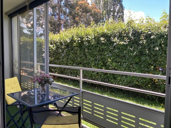 A balcony with a glass table and chairs, a vase with flowers, and a view of a hedge and trees. - Nice 86m² With Terrace Near The Beach! (Arcachon)