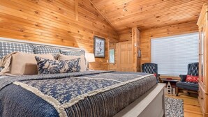 Une chambre dans une cabane en bois, avec un lit, une chaise, une petite table et une fenêtre avec des stores.