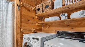 Une buanderie équipée d’un lave-linge et d’un sèche-linge à chargement frontal, d’étagères en bois où sont rangées des serviettes et de paniers.