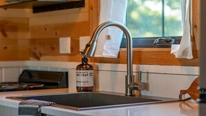 A modern kitchen with a stainless steel sink, wooden wall paneling, and a window with a view of greenery.