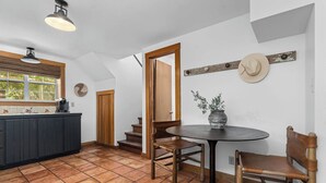 A kitchen with a large island, wooden chairs, a round table, and a rustic hat on the wall.