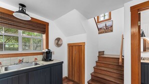 A kitchen with a wooden staircase, a window with blinds, a sink, and a coffee maker.