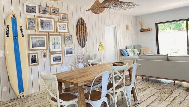 Un coin repas avec une table en bois et des chaises blanches, agrémenté de photographies encadrées accrochées au mur.