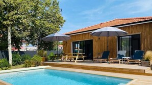 Une piscine rectangulaire avec une terrasse en bois, entourée de chaises longues et de parasols.