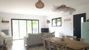 Un salon moderne avec un canapé, une table à manger et des chaises. On peut voir une télévision et une porte.