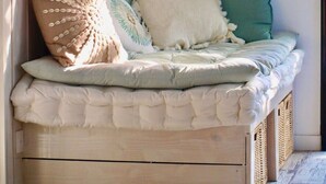 Une pièce chaleureuse et bien éclairée, avec un banc-lit en bois, une étagère ornée d’objets décoratifs et un interrupteur fixé au mur.
