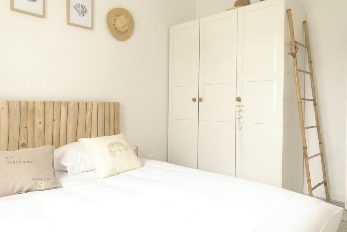 A bedroom with a wooden headboard, a bed with white bedding, a wardrobe, and a ladder against the wall.