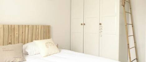 A bedroom with a wooden headboard, a bed with white bedding, a wardrobe, and a ladder against the wall.
